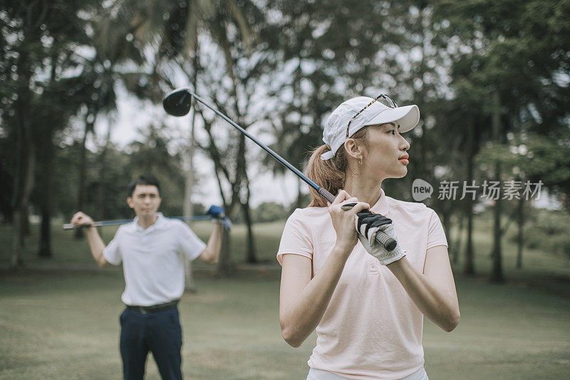 asian chinese female golfer teeing off at golf course with her husband beside